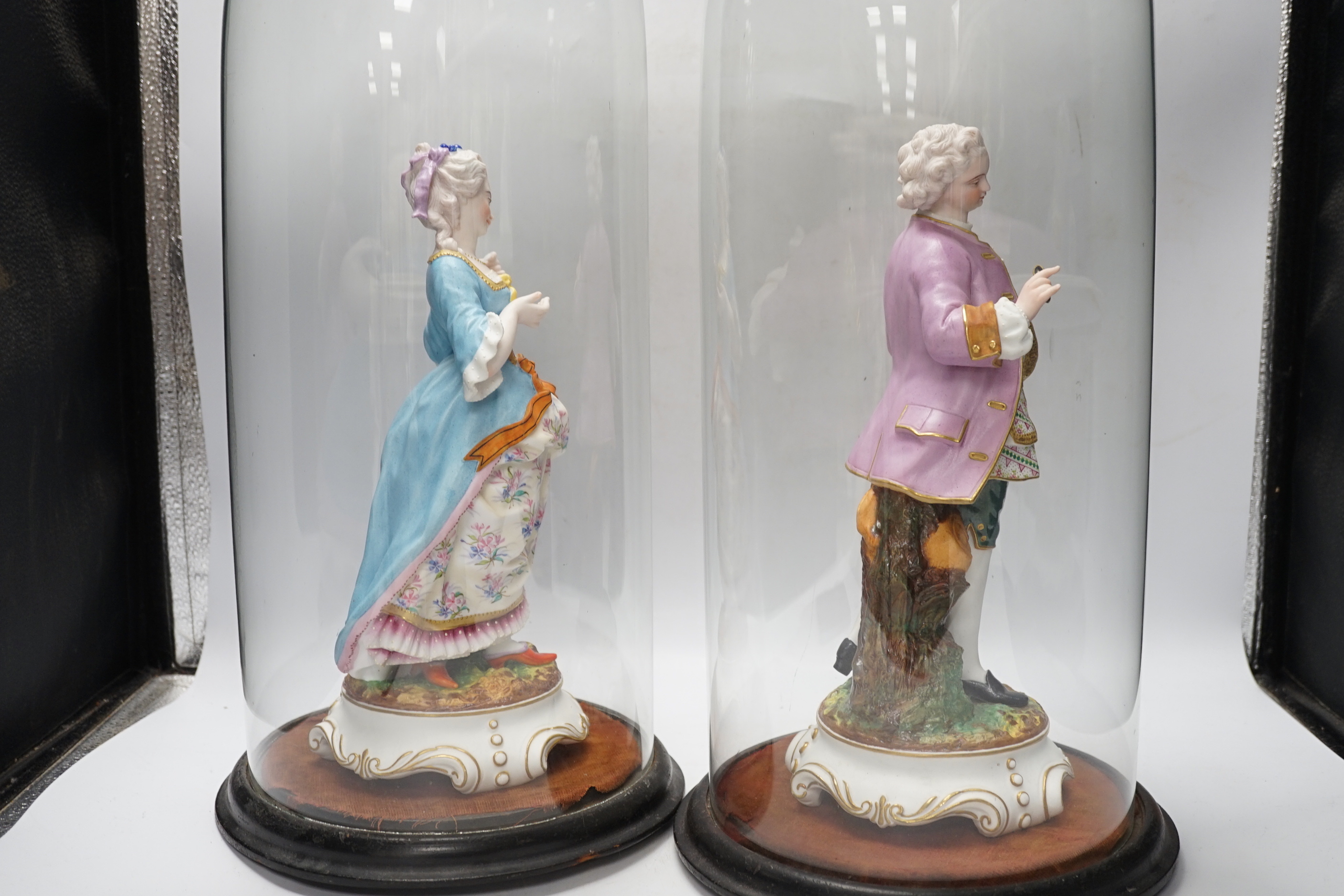 A pair of continental bisque porcelain figures, under glass domes, 48cm overall
